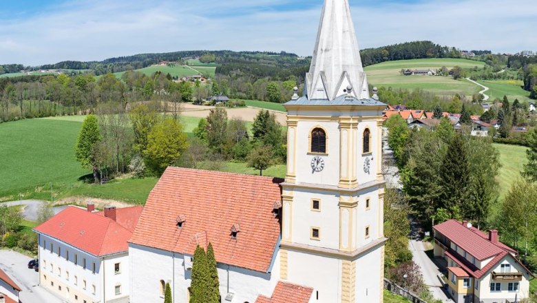 Aerial view of the fortified church of Krumbach in a rural setting with green fields and blue sky.