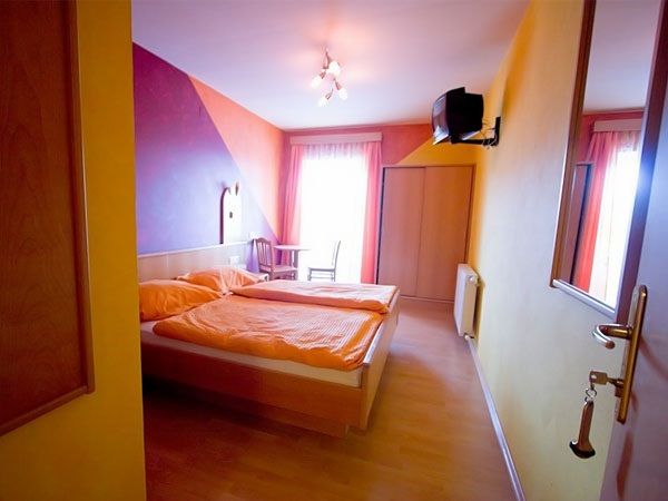 A cozy guest room with a double bed, colorful walls and a small TV on the wall.