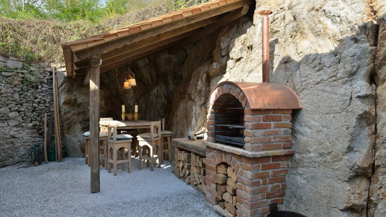 Rustic outdoor area with brick oven and wooden table under a wooden roof.