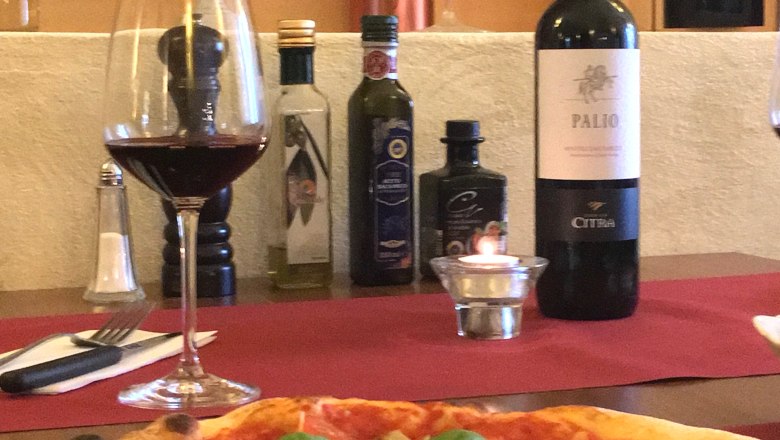 Pizza with basil and parmesan on a table with red wine and olive oil.