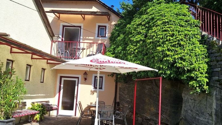 A cozy garden with a parasol, table and chairs in front of a house with a balcony and green climbing plants.