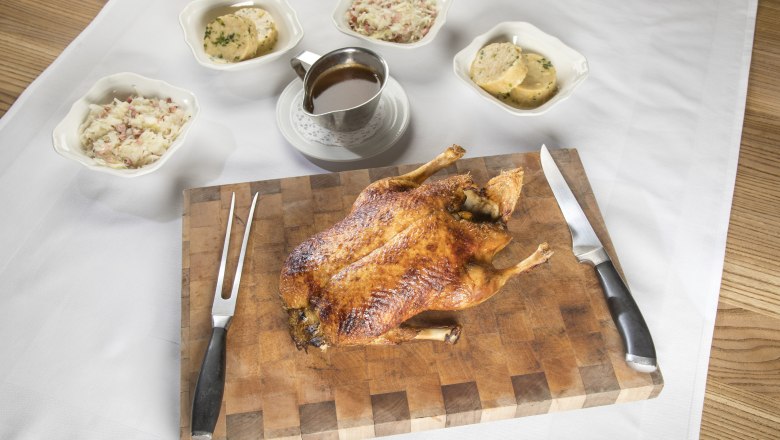 Baked duck on a wooden board with side dishes and sauce.