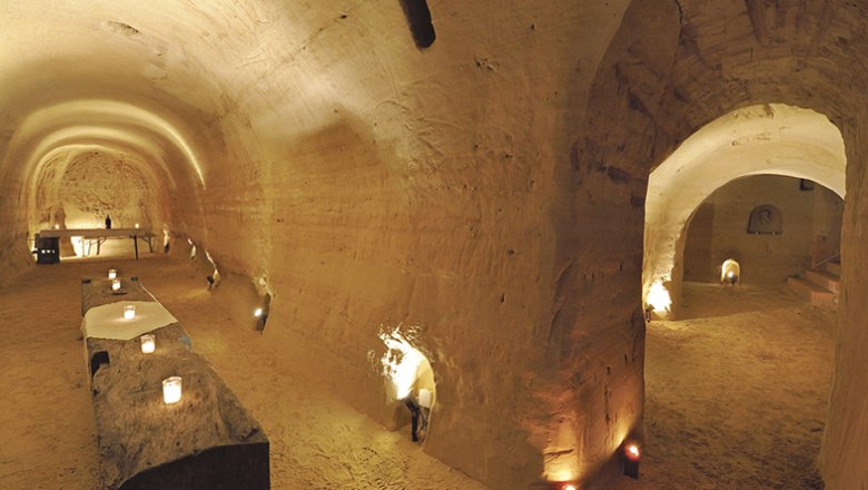 Underground sandstone cellar with candlelight and rustic tables.