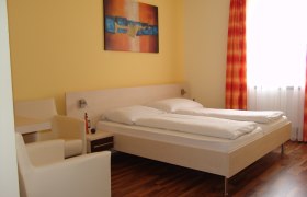 A modern hotel room with a double bed, yellow walls and an abstract painting.