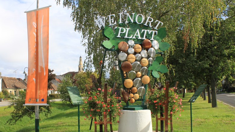 Welcome sign in Platt with grape decoration and church in the background.