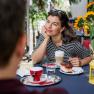Woman in striped shirt enjoying coffee and cake outdoors, surrounded by sunflowers.