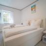 Modern bedroom with double bed, white bed linen, mural, window with curtains and flat screen TV.