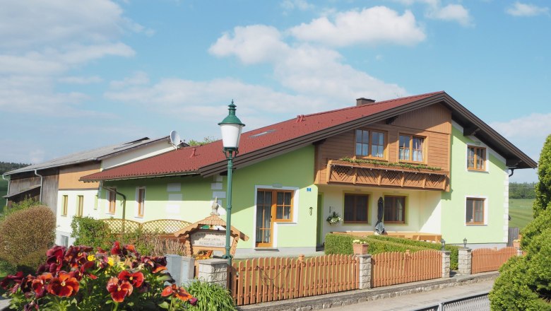 A vacation farm with green paint and wooden balcony, surrounded by a wooden fence and flowers in the foreground.