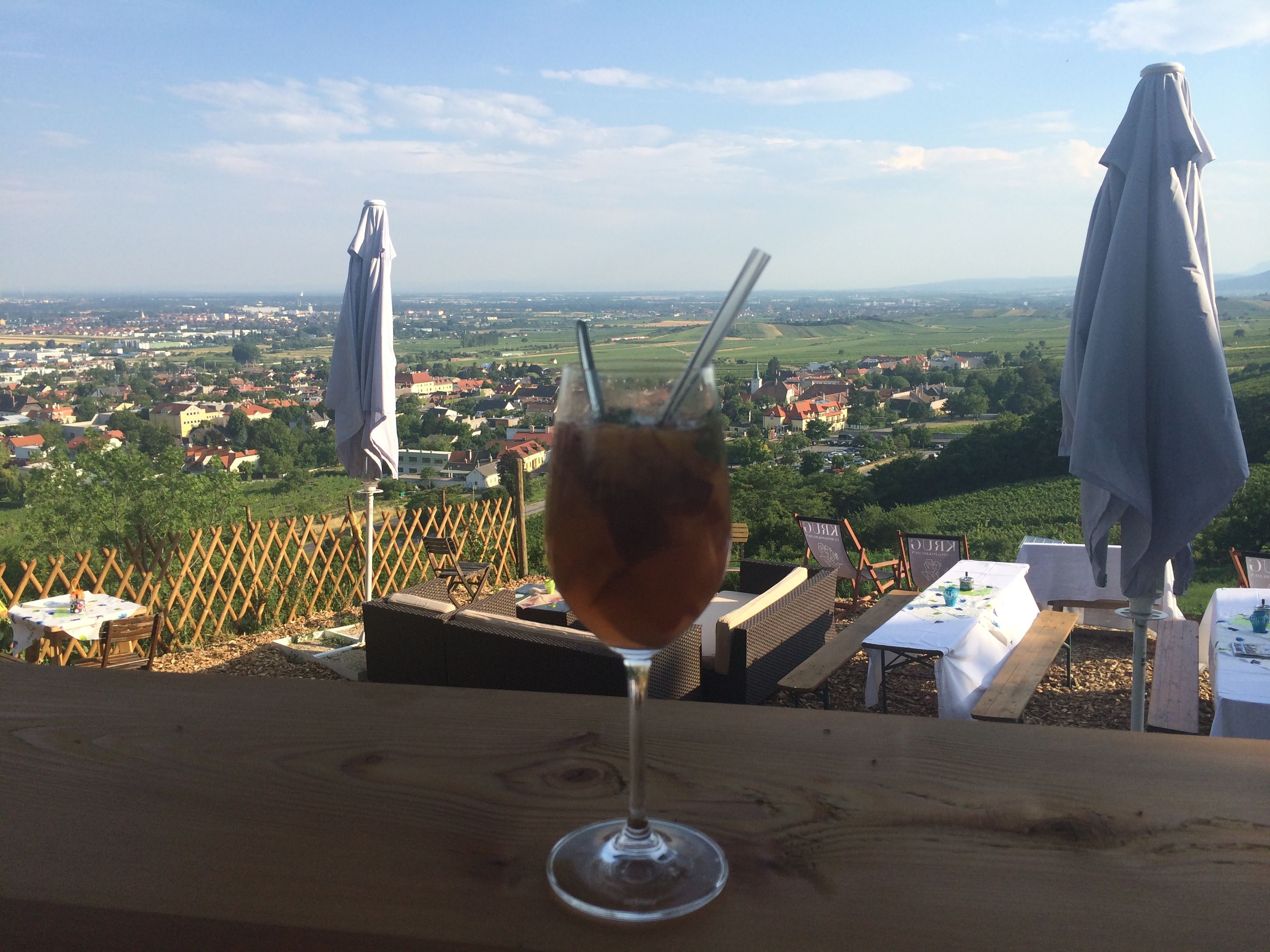 A drink in a wine glass with straws in front of a landscape of tables and parasols.