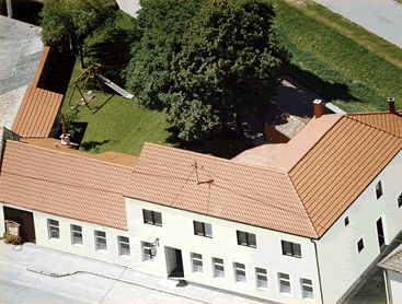 Aerial view of a building complex with red roof and inner courtyard with trees and playground.