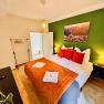 Cozy bedroom with green painted wall, double bed with red pillows, bedside tables and lamp.