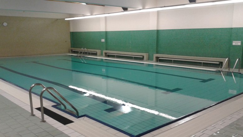 Interior view of an empty indoor pool with green tiled walls and a large swimming pool.