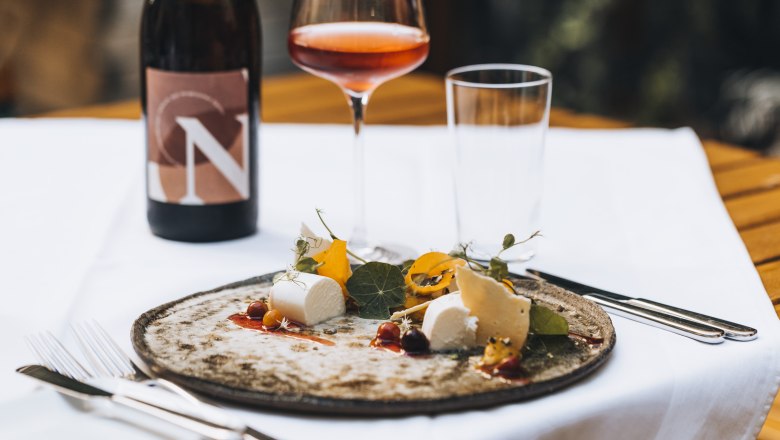 A plate with cheese and garnish, a glass of rosé wine and a bottle of wine on a table.