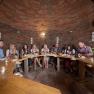 Group of people sitting at a wooden table in a wine cellar.