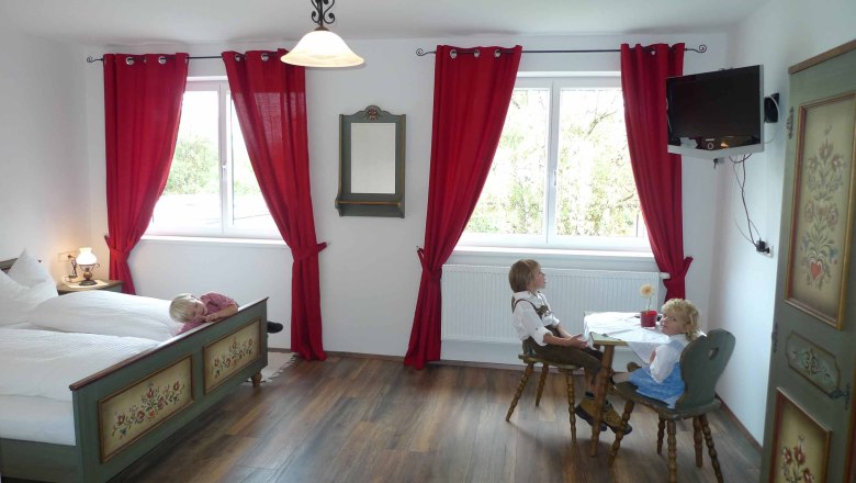 A traditionally furnished room with a wooden floor, red curtains and a table with two dolls in traditional costume.