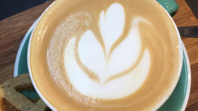 Cappuccino with latte art in a green cup on a wooden board.