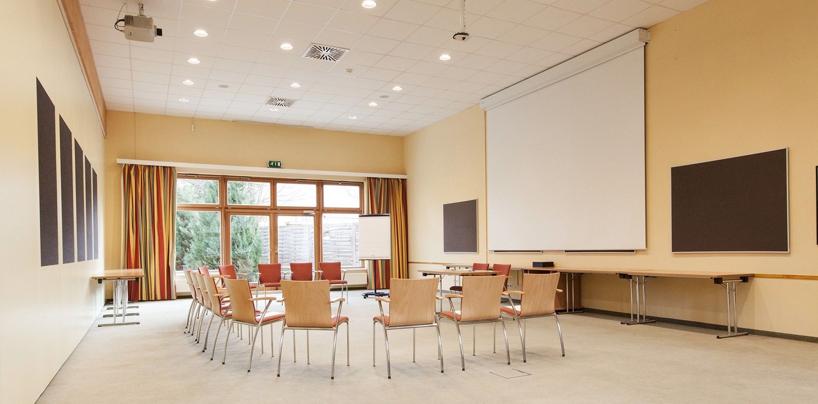 An empty seminar room with a circle of chairs, projector, screen and flipchart.