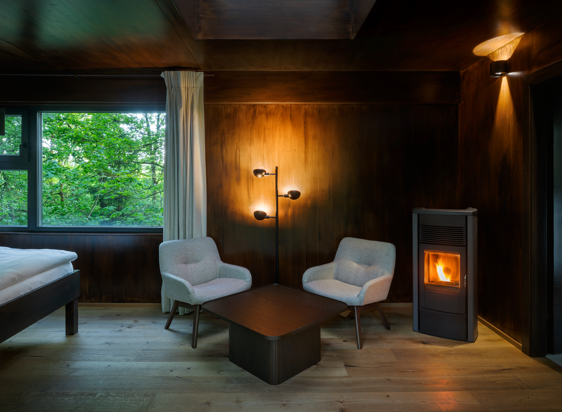 Interior view of a cozy tree house with two armchairs, a table and a wood-burning stove.
