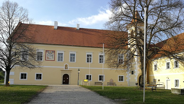 Yellow castle building with red roof and tower, surrounded by trees.