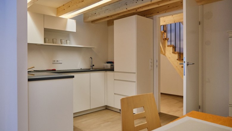 Modern kitchen with white cupboards, wooden ceiling and open access to a staircase.