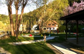 Miniature golf course with trees and a building in the background.