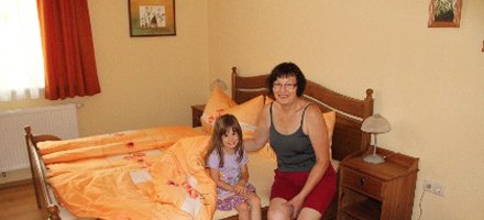 A woman and a child are sitting on a bed in a guest room with orange bed linen.