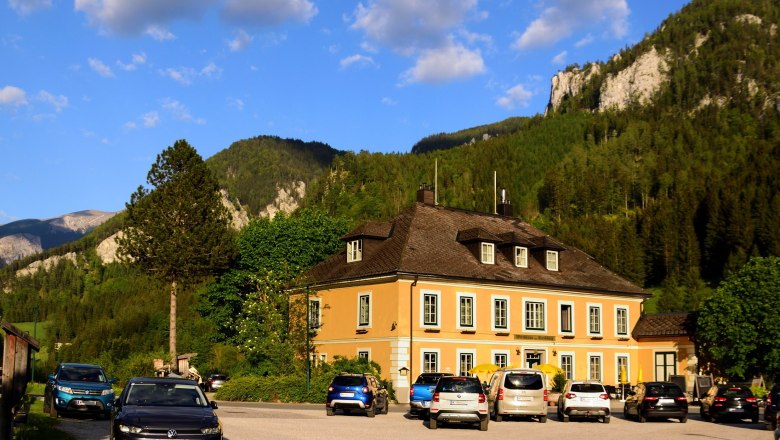 A yellow building against a mountain backdrop with parked cars in front of it.