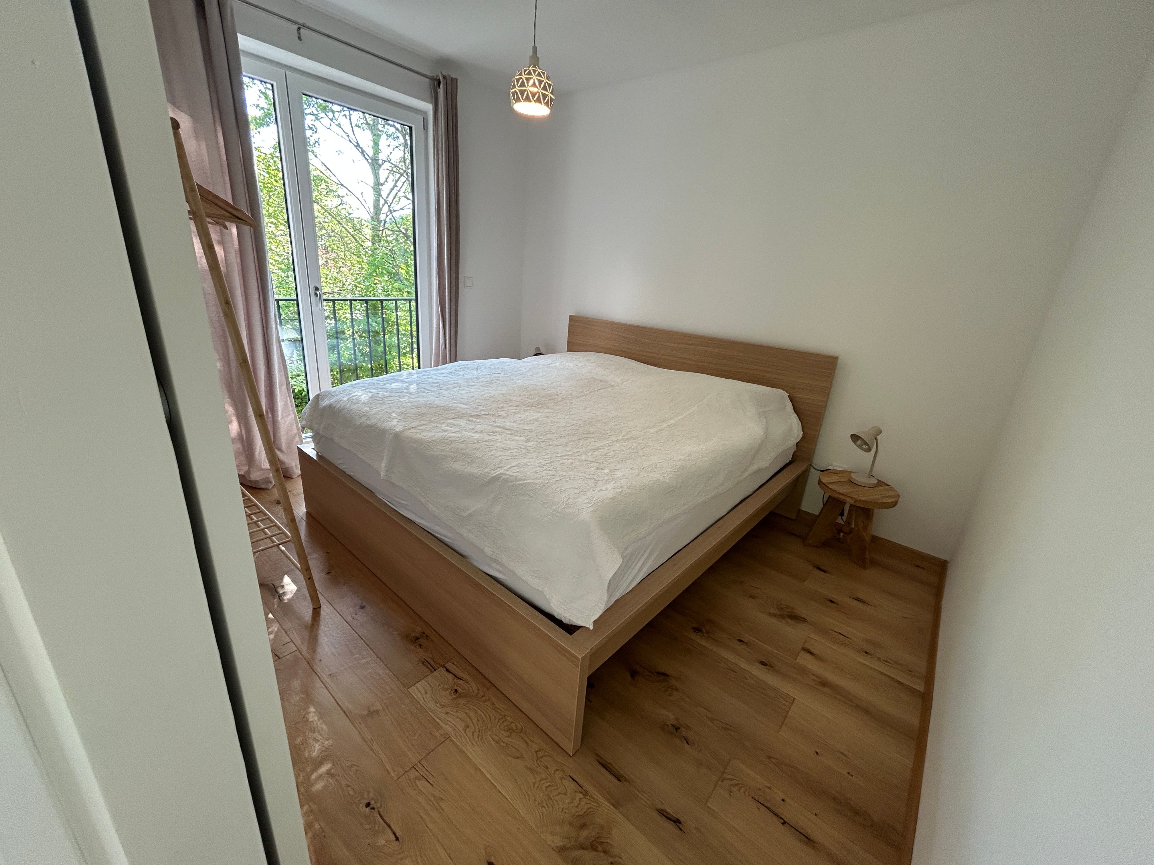 Bedroom with wooden floor, double bed and window with view of the greenery.