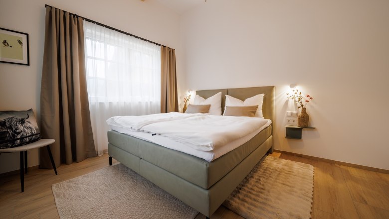 Modern bedroom with double bed, wooden floor and large windows with curtains.