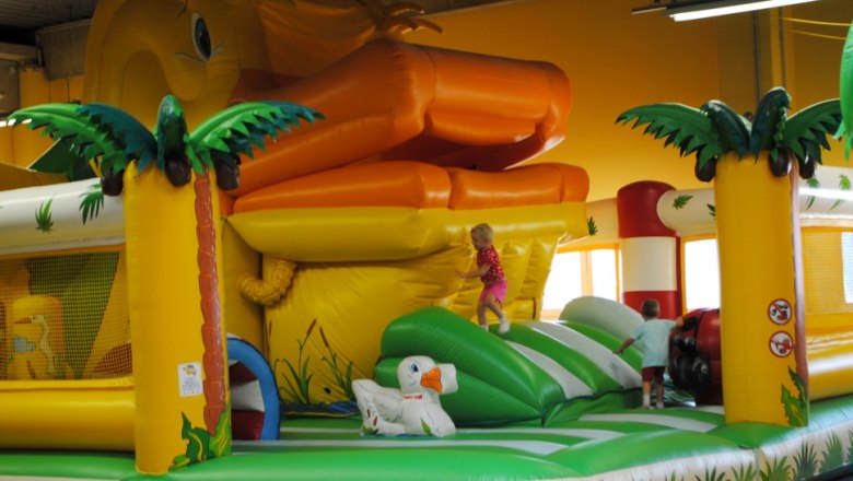 Inflatable bouncy castle with giant duck and palm trees, children play on it.