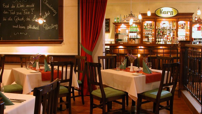 Cozy restaurant with wooden furniture, set tables and a bar in the background.