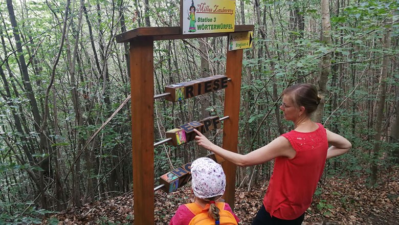 Two people at a station in the forest with word cubes on Milla's magic trail.