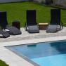 Four black sun loungers by the pool on a paved area in the garden.