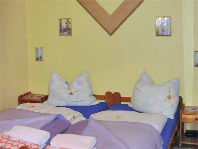 Two single beds in a room with a yellow wall and decorative pictures.