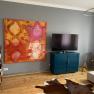 Living room with large colorful painting, TV on blue cabinet, wooden floor and cowhide carpet.