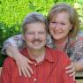 A smiling couple sits on a bench in the garden.