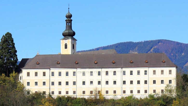 Gloggnitz Castle in front of wooded hills and a blue sky.