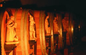 Row of wooden barrels with carved figures in a wine cellar.