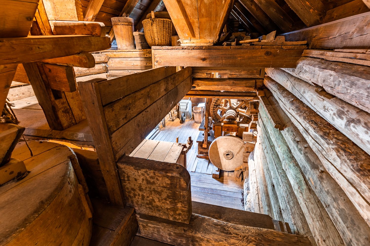Interior view of an old mill with wooden structures and millstone.