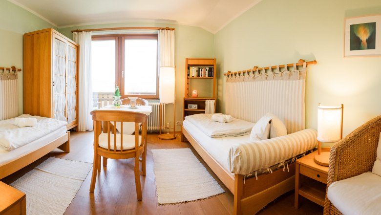 Comfortable twin room with wooden furniture, two beds, table, chairs and a window with curtains.