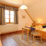 Cozy guest room with wooden furniture, double bed, small table and chairs, TV and window with curtains.