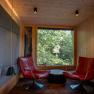 Interior view of a modern tree house lodge with two red armchairs in front of a large window with a view of the forest.