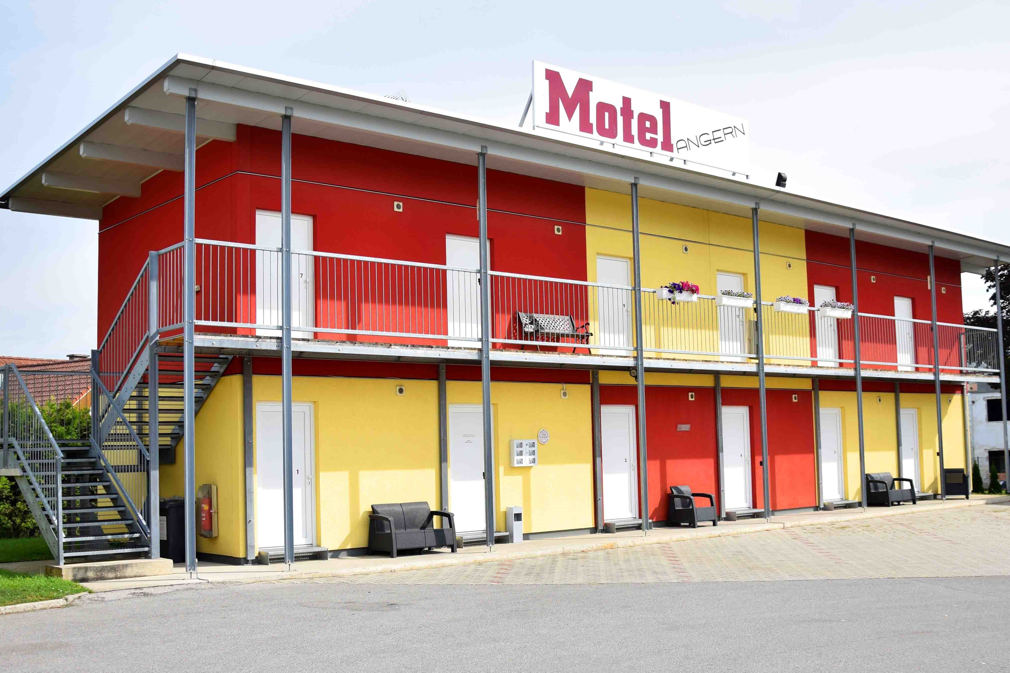 Two-story motel building with yellow and red walls, stairs and balcony.