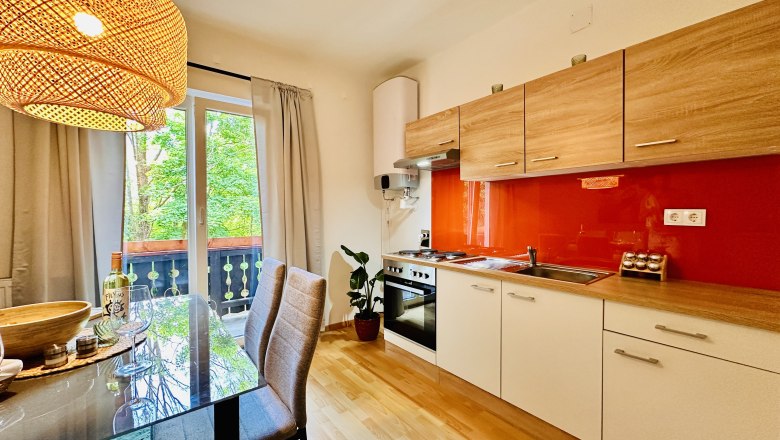 Modern kitchen with wooden units, red splashback and dining table in front of a window with a view of the greenery.