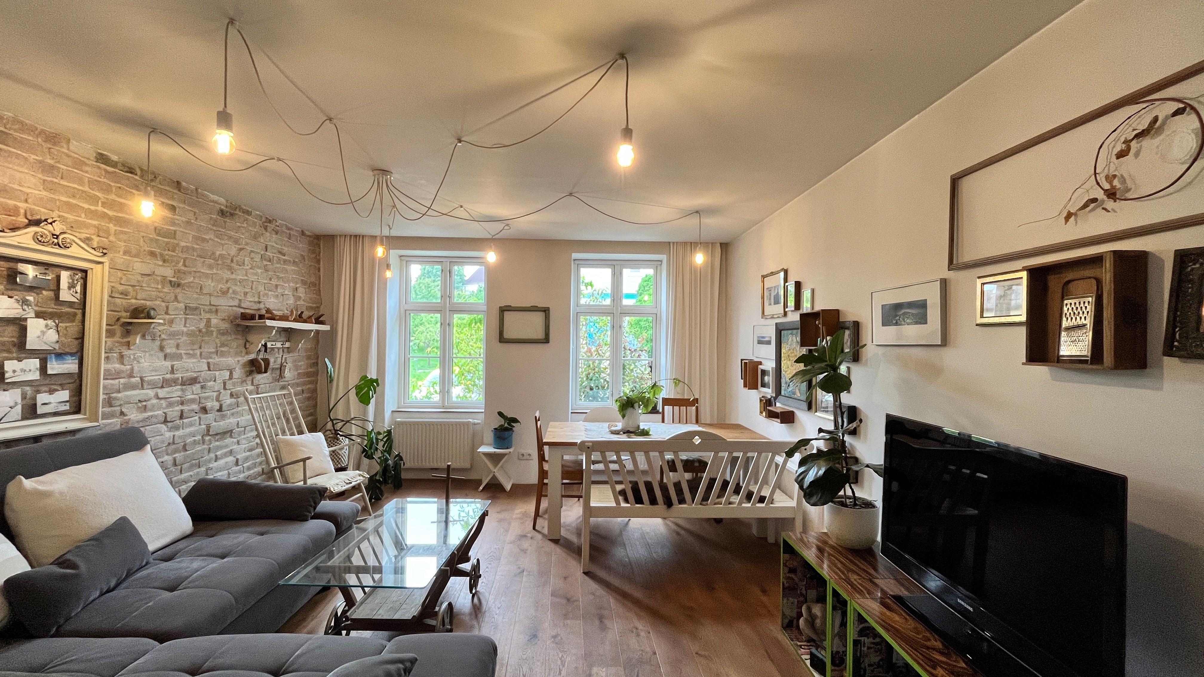 Cozy living room with grey sofa, wooden table, plants and wall decorations.