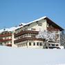A large, traditional building in the snow with wooden decorations and a snow-covered tree in front of it.