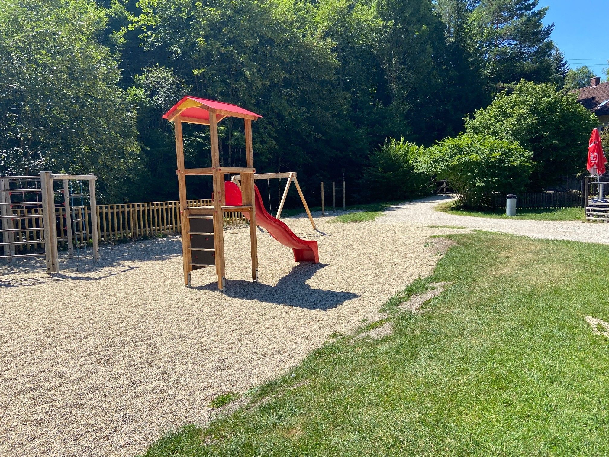A children's playground with slide and climbing frame, surrounded by trees and lawn.