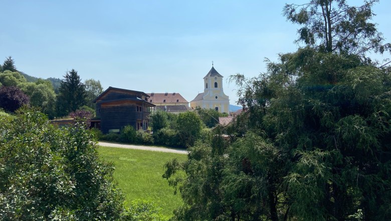 View of a church and a wooden house behind trees and meadows.