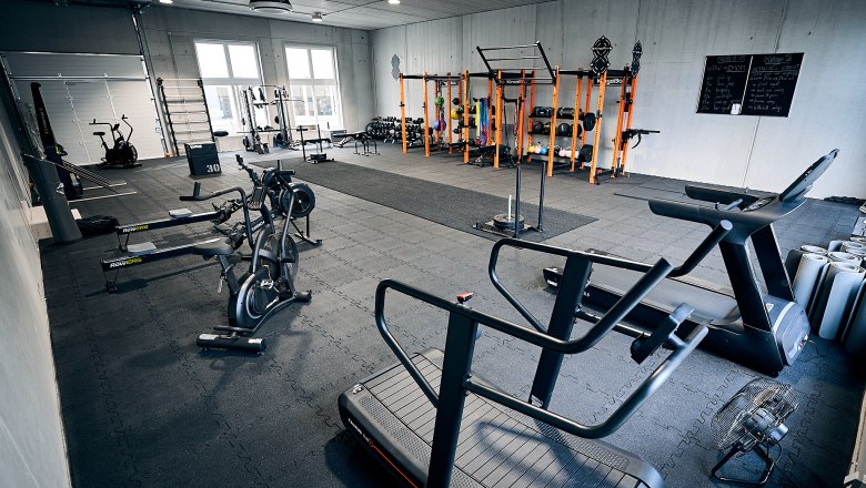 Interior view of a fitness studio with various training equipment such as treadmills, bicycles and dumbbells.