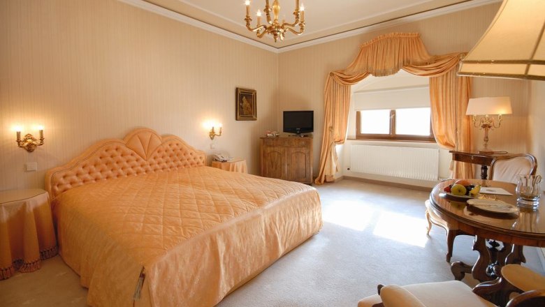 Elegant guest room with large bed, chandelier and table with fruit.